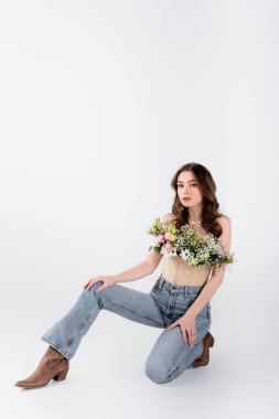 Genç model kot pantolon, ayakkabılar ve çiçekler gri arka planda.