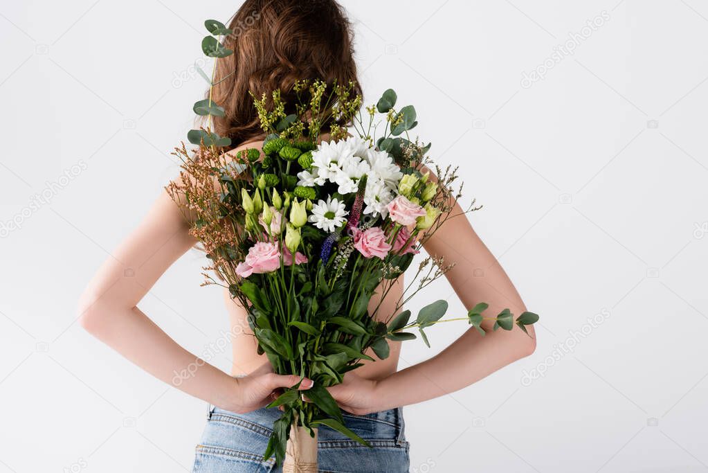 Back view of model in jeans holding flowers isolated on grey 