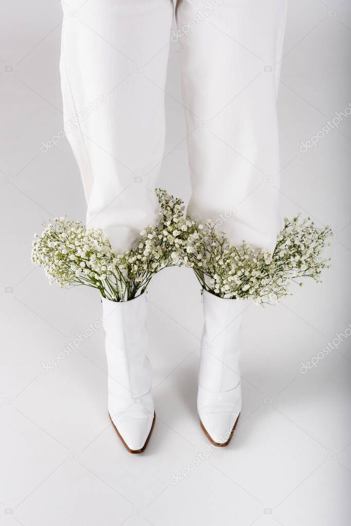 Cropped view of woman with baby breath flowers in shoes on grey background