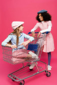 módní mezirasové dívky při pohledu na sebe, zatímco se baví s nákupním vozíkem na růžové