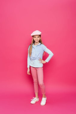 Moda elbiseli kız kameraya gülümserken ellerin pembe üzerinde poz veriyor.