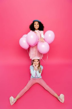 Mutlu Afro-Amerikalı kız moda arkadaşının yanında pembe balonlarla oturuyor. 