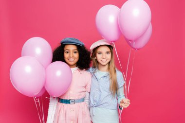 İki mutlu, çok kültürlü bahar kıyafetli kız pembe renkli balonlarla poz veriyorlar. 