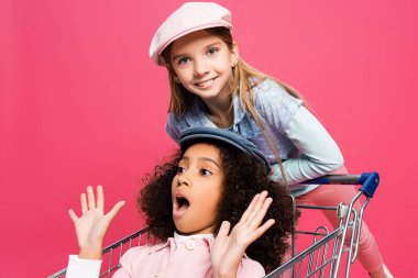 Mutlu kız kameraya bakıyor. Pembe alışveriş arabalı afro-amerikan çocuğun yanında.