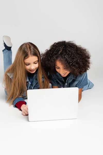 Cheerful Interracial Friends Denim Clothes Using Laptop While Lying Grey — Stock Photo, Image