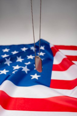 Amerikan bayrağı yakınındaki künyenin yakın görüntüsü gri arkaplanda bulanıklaştı 