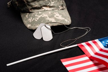 Close up view of dog tags, cap and american flag on black background  clipart