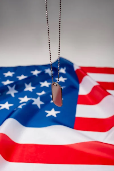 Close up view of dog tag near american flag blurred on grey background