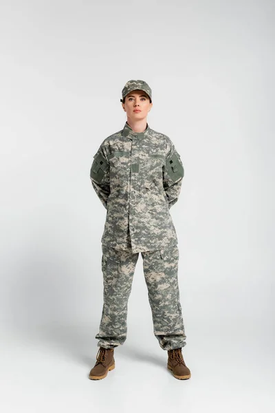 Woman in military uniform and boots looking at camera on grey background