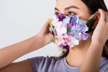 Tıbbi maske takan genç bir kadın çiçek açmış ve beyaz üzerinde izole edilmiş.
