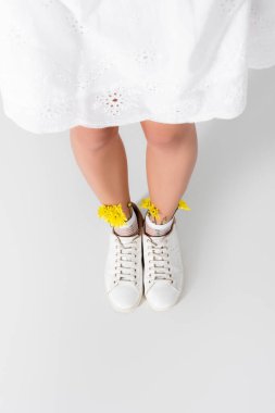 Yüksek açılı spor ayakkabılı model, beyaz üzerinde sarı kır çiçekleri poz veriyor.