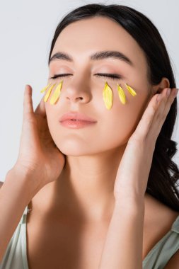 Yüzünde sarı taç yaprakları olan genç bir kadın beyaz bir odada izole edilmiş.