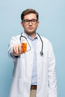 Gözlüklü doktor ve elinde ilaç şişesi olan beyaz önlüklü doktor mavi arka planda izole edilmiş.