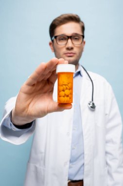 bottle with medication in hand of doctor on blurred background isolated on blue clipart