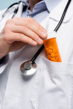 cropped view of doctor in white coat with stethoscope putting bottle with medication in pocket  clipart