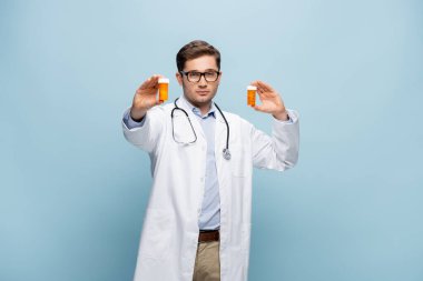 Doktor gözlüklü ve beyaz önlüklü elinde ilaç şişeleri olan mavi üniformalı.