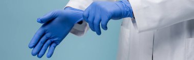 Beyaz önlüklü, lateks eldivenli, mavi pankarttaki doktorun kısmi görüntüsü