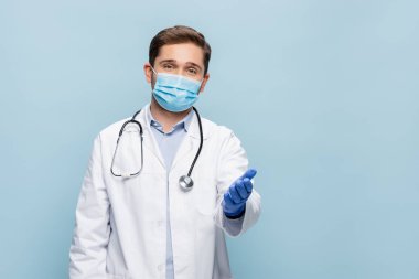 Tıbbi maskeli doktor ve steteskoplu beyaz önlüklü doktor mavi üzerine el izole edilmiş.