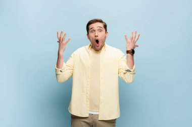Şok olmuş genç adam kameraya bakıyor ve maviye işaret ediyor.