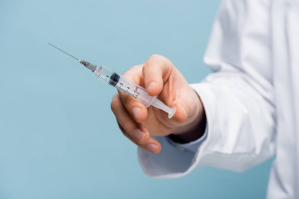 cropped view of doctor holding syringe in hand isolated on blue