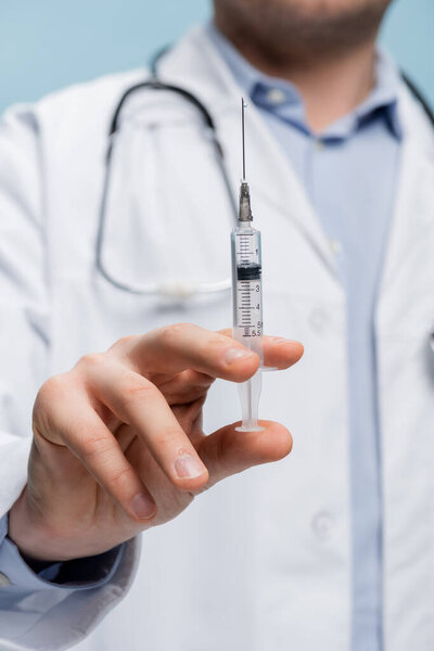 partial view of doctor holding syringe isolated on blue