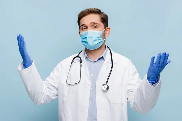 医療用マスクの若い医師と青で隔離された卓越した手で立っている白いコート — ストック写真