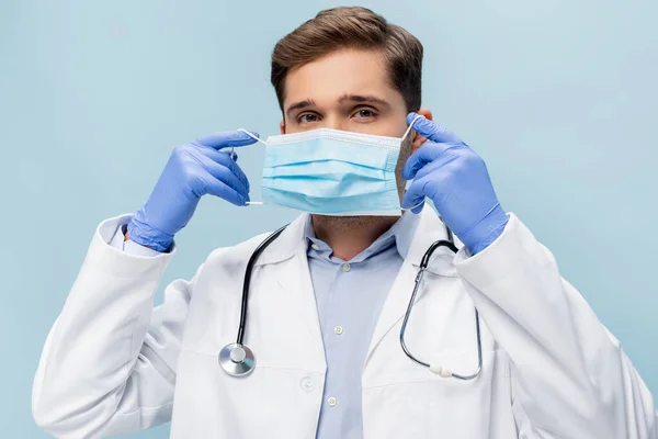 Młody Lekarz Białym Płaszczu Stetoskopem Noszący Maskę Medyczną Odizolowaną Niebiesko — Zdjęcie stockowe