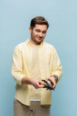 happy young man in yellow shirt holding wallet with dollars isolated on blue