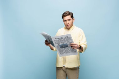 Sarı gömlekli genç adam mavi üzerine seyahat gazetesi okuyor.