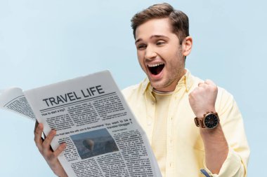 Tişörtlü genç adam seyahat gazetesi okuyor ve mavi üzerine izole edilmiş seviniyor.