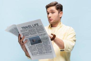 Gömlekli genç adam mavi üzerine izole edilmiş seyahat gazetesi okuyor.