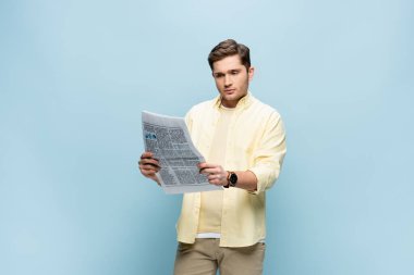 Gömlekli genç adam mavi üzerine gazete okuyor.