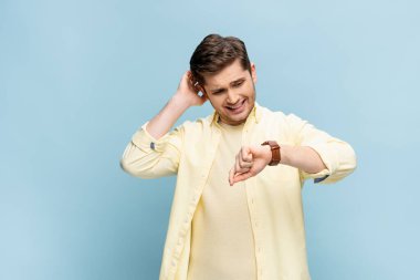 worried young man in yellow shirt looking at wristwatch on blue clipart