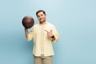 Sarı tişörtlü mutlu adam mavi gömlekli basketbolu işaret ediyor.