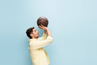 Sarı gömlekli bir adamın maviliğe basketbol topu atması.