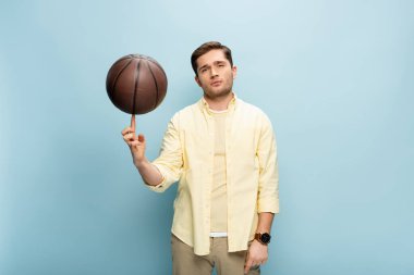 Sarı gömlekli oyuncu basketbol topunu mavi parmağında döndürüyor.