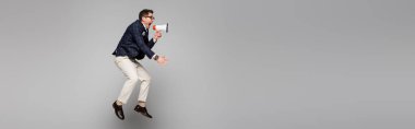 full length of businessman jumping and screaming in megaphone on grey, banner clipart