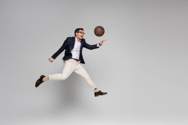 Tam uzunlukta neşeli bir iş adamı gride havada süzülürken basketbol oynuyor.