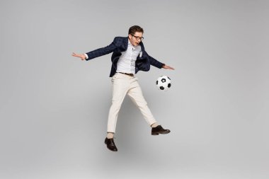 Tam uzunlukta neşeli bir iş adamı, gri üzerinde havada süzülürken futbol oynuyor.