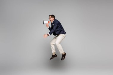 full length of screaming in megaphone while levitating on grey  clipart