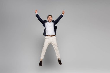 full length of excited man with outstretched hands jumping on grey clipart