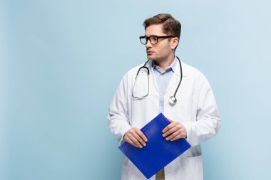 Endişeli doktor gözlüklü, beyaz önlüklü, elinde not panosu olan mavi gözlüklü.