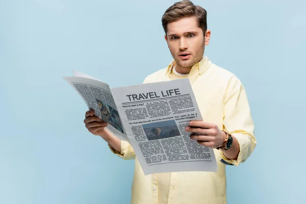 astonished man reading travel newspaper isolated on blue