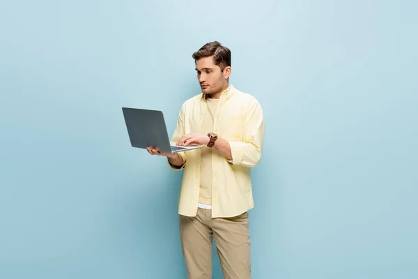 young man in yellow shirt using laptop isolated on blue
