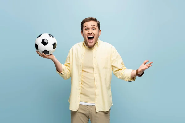 amazed man in yellow shirt holding football on blue
