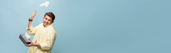 sick man throwing napkin away and holding tissue box isolated on blue, banner