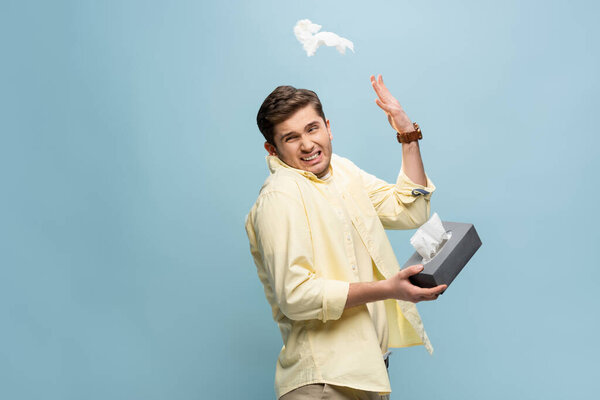 sick man throwing away napkin and holding tissue box isolated on blue