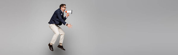 full length of businessman jumping and screaming in megaphone on grey, banner