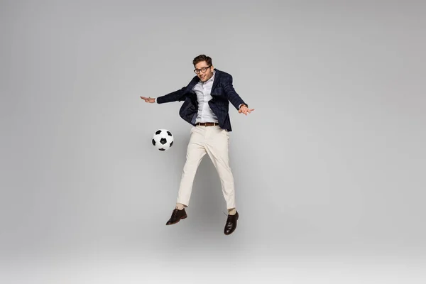 full length of smiling businessman playing football while levitating on grey