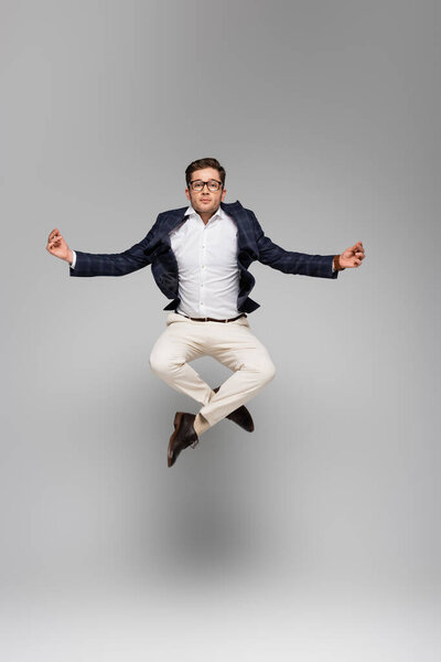 full length of businessman in glasses meditating and levitating on grey
